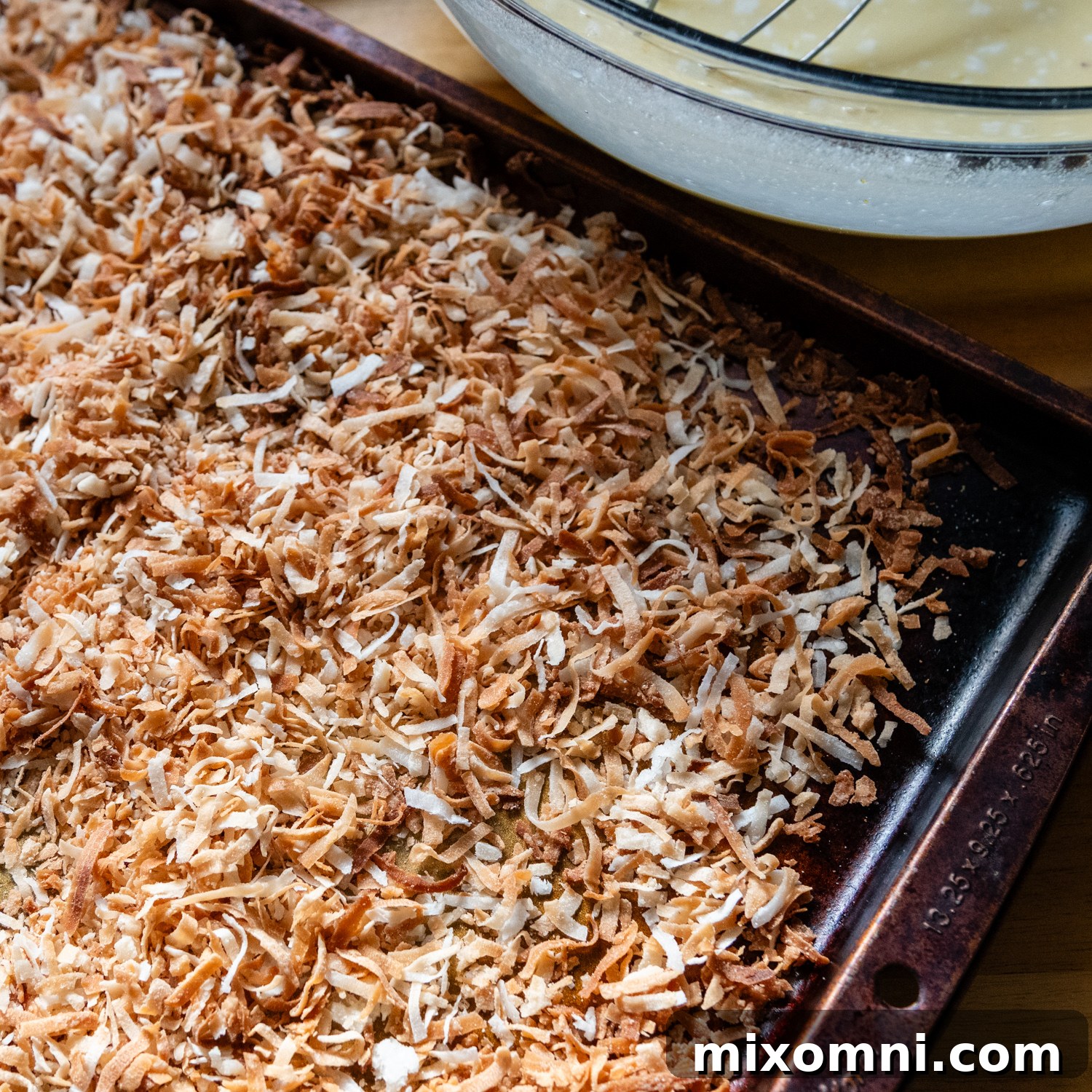 The flan mixture in a glass bowl, now with toasted shredded coconut mixed in, ready to be poured over the hardened caramel in the baking pan.