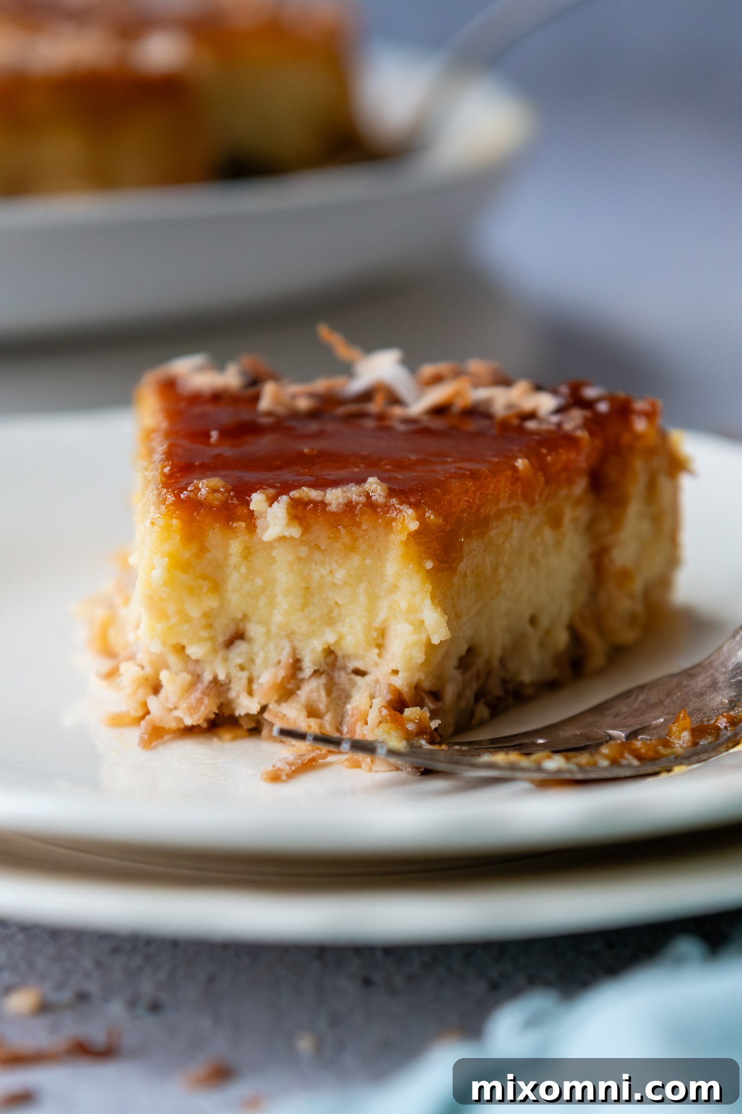 A close-up view of a slice of coconut flan, revealing the distinct layers of caramel, creamy coconut custard, and the delightful toasted coconut crust at the bottom.