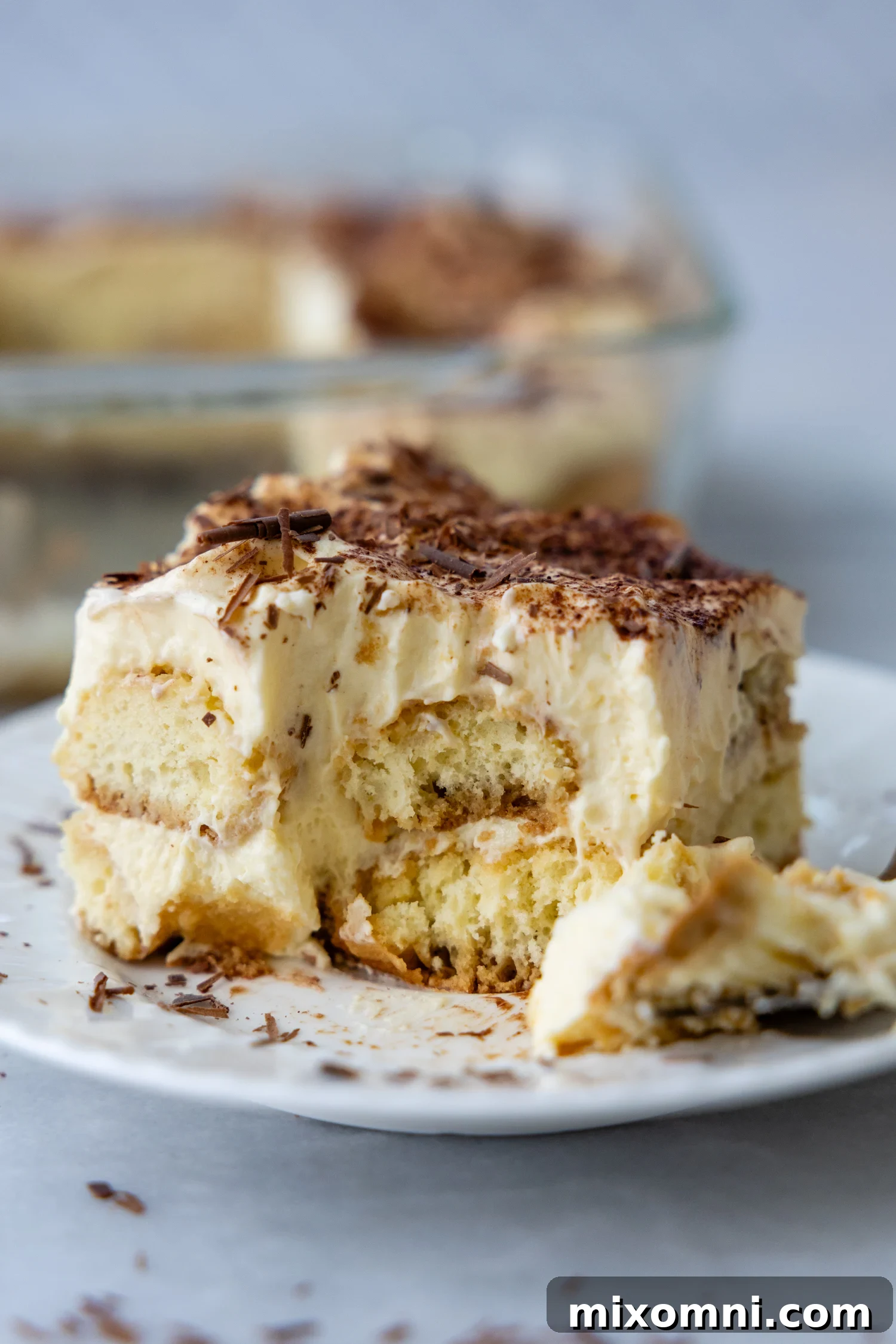 A slice of tiramisu with a bite taken out of it, showing distinct layers of cream and coffee-soaked ladyfingers.