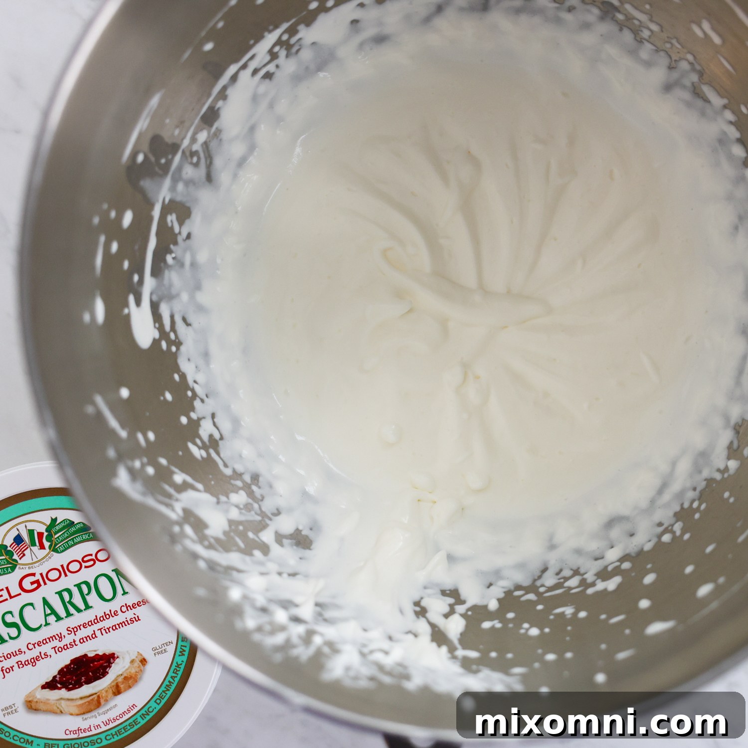 Heavy cream and mascarpone mixture being whipped in a mixing bowl, showing a smooth, creamy texture.