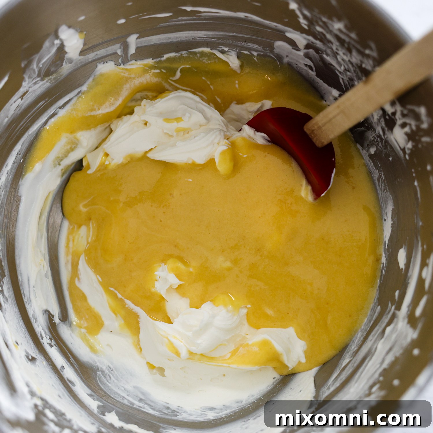 The cooked egg custard being gently folded into the mascarpone and whipped cream mixture in a large bowl.