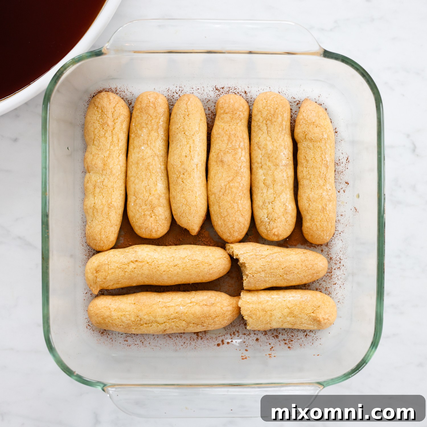 Espresso-dipped ladyfingers arranged in a single layer at the bottom of a glass baking dish.