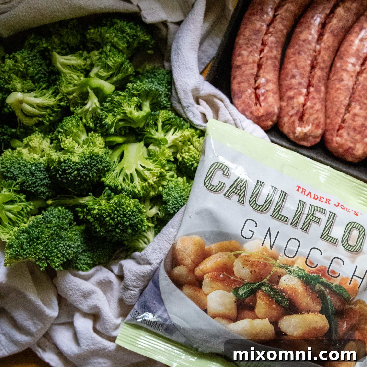A vibrant selection of simple ingredients laid out on a kitchen counter: frozen gnocchi, fresh broccoli florets, sweet Italian sausage, olive oil, garlic, and salt.