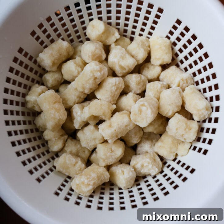 Frozen gnocchi resting in a colander, allowing ice crystals to melt and drain away before roasting.