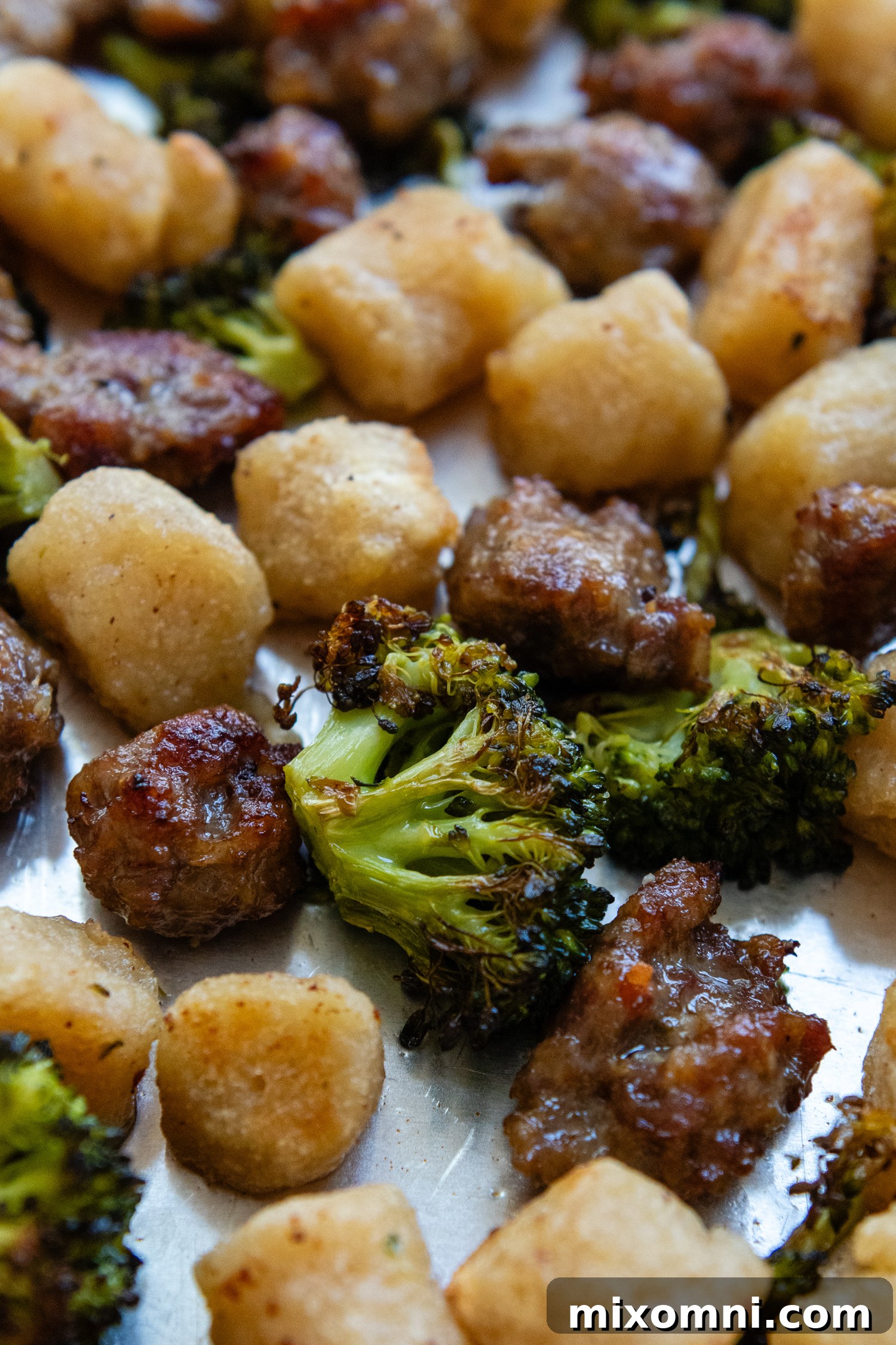 Close up of a bountiful sheet pan filled with perfectly cooked crispy gnocchi, roasted broccoli, and crumbled Italian sausage, ready for serving.