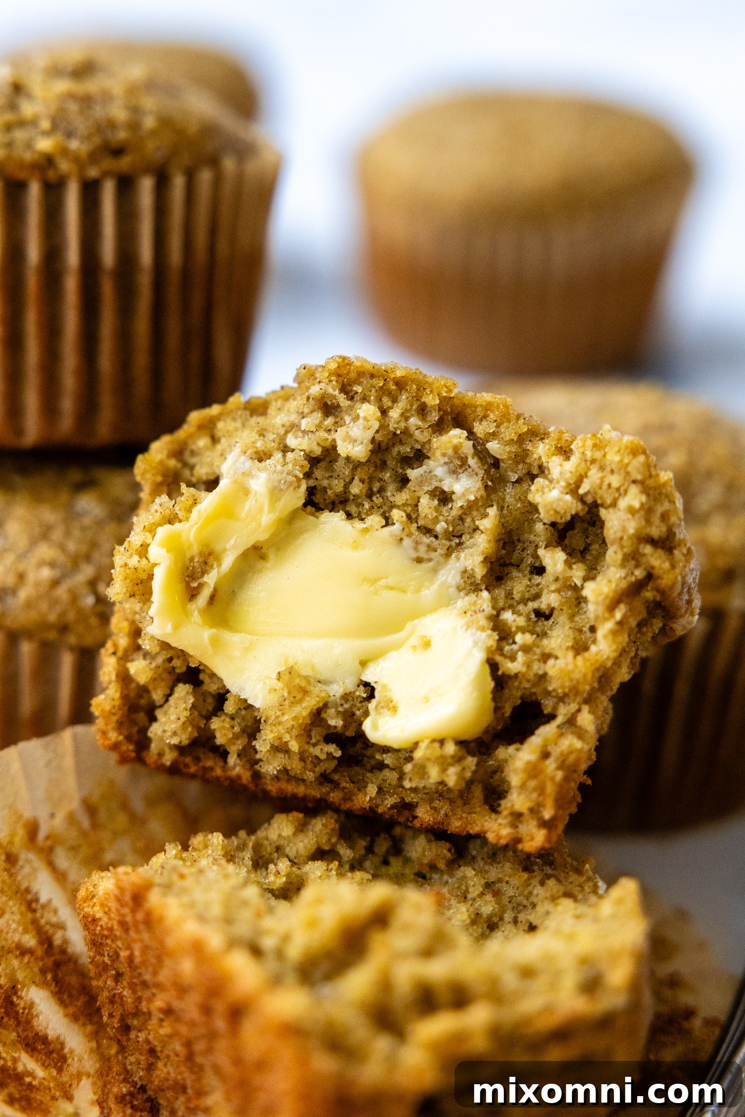 A freshly baked banana oat muffin cut open, revealing its moist interior, with a dollop of butter melting on top.