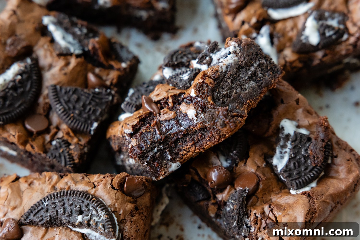A brownie on top of other brownies with a bite taken out, showing the fudgy interior and Oreo chunks.