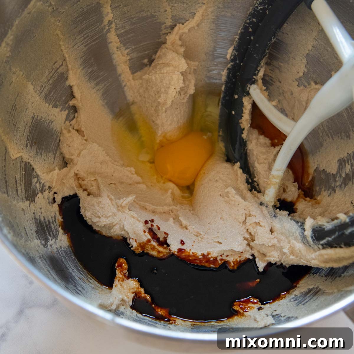 Gluten-free cookie dough with egg and molasses being incorporated into the light and fluffy creamed butter and sugar mixture, ready for dry ingredients.