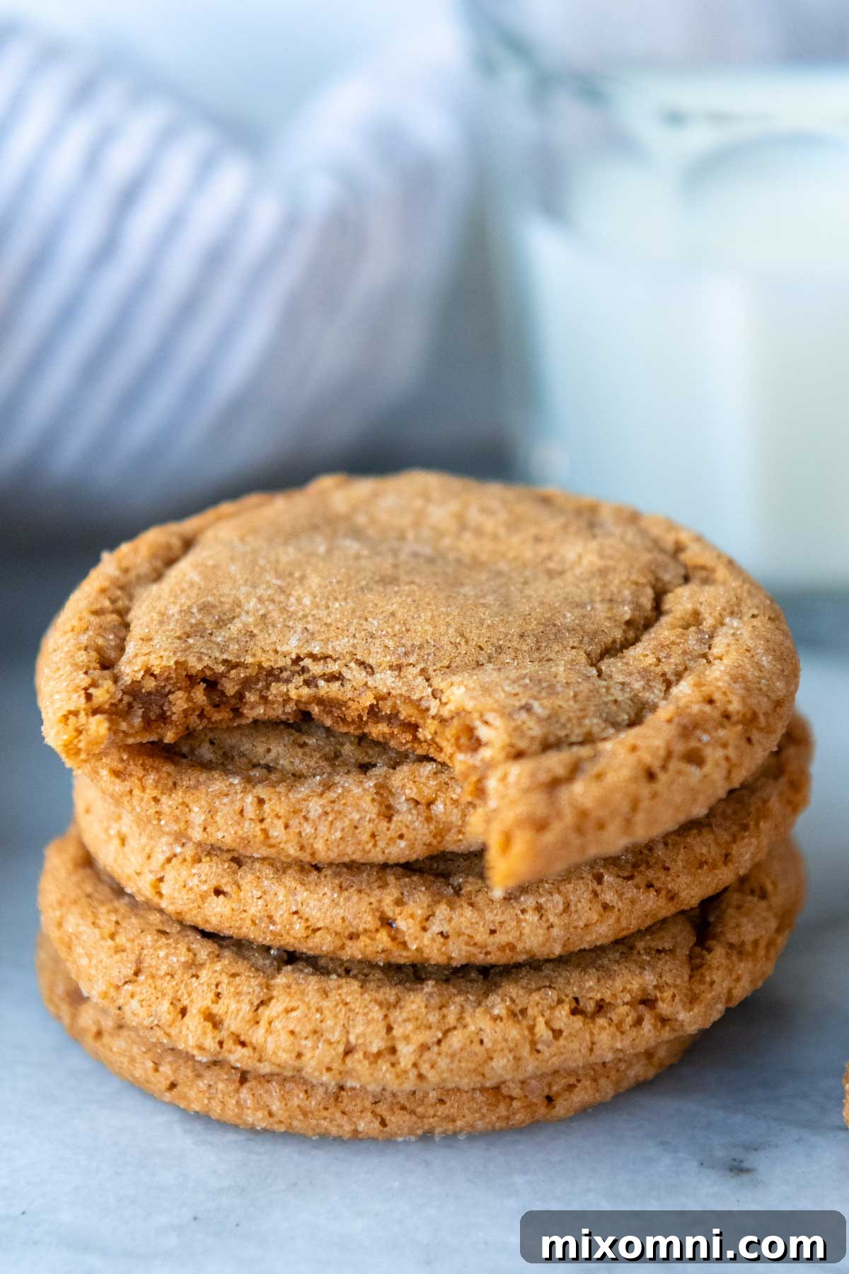A delectable stack of soft and chewy gluten-free ginger snap cookies, beautifully baked with a classic crinkled top, with one cookie showing a tempting bite taken out.