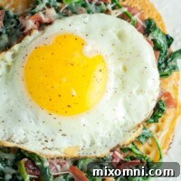 overhead shot of spinach, egg, prosciutto socca pizza on a white plate