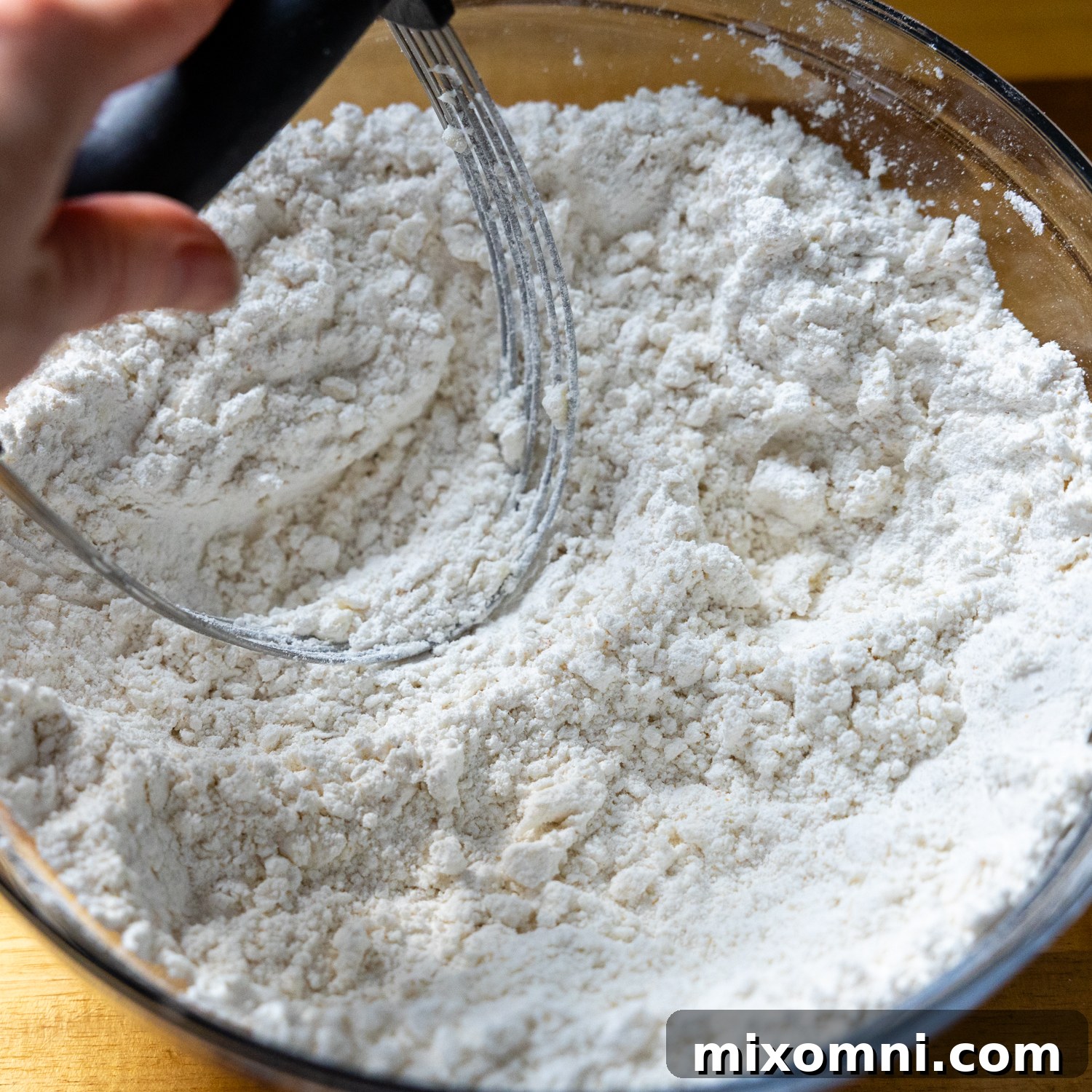 Cold butter being cut into a bowl of dry biscuit ingredients with a pastry blender.