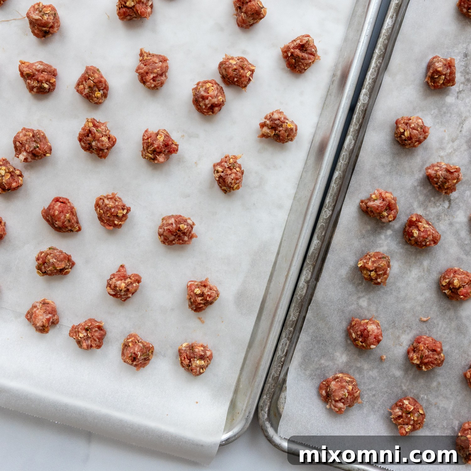 Meatballs on parchment paper on baking sheet, ready for the oven.