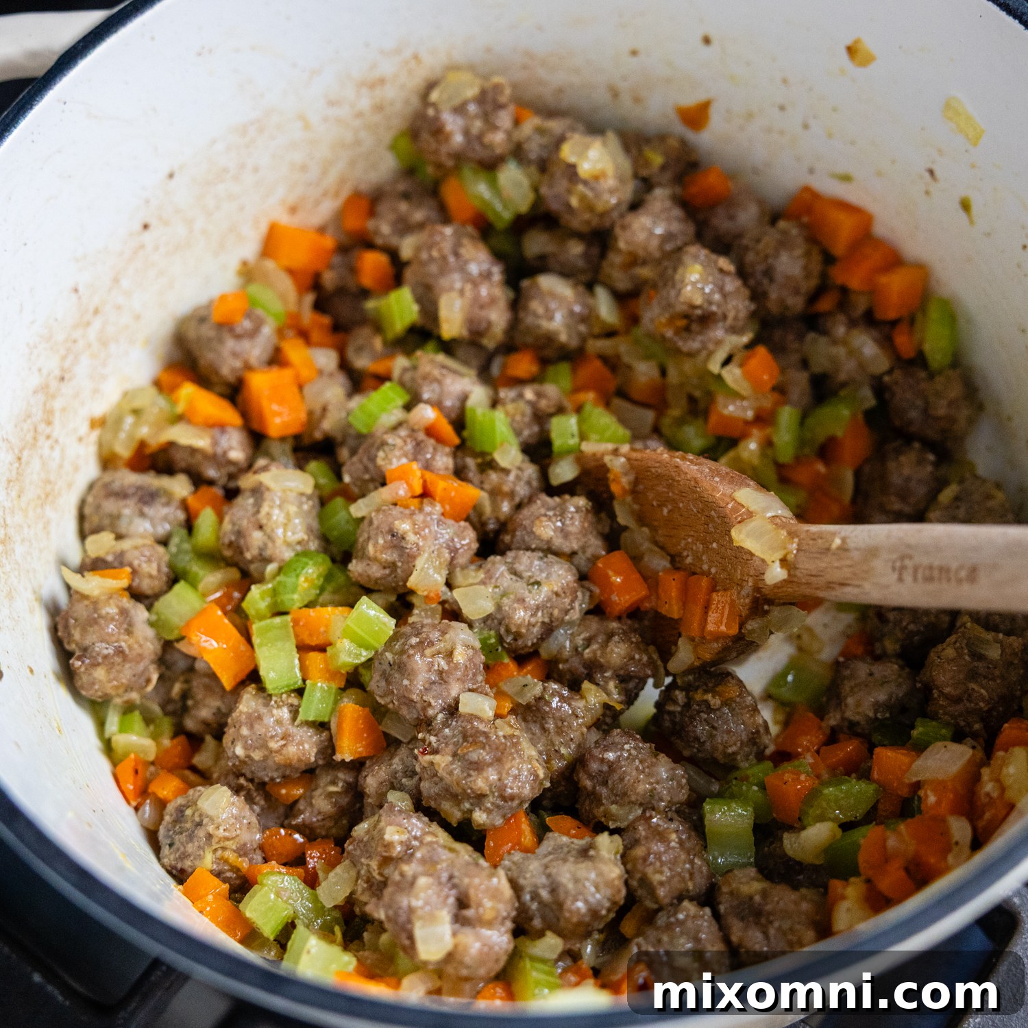 Cooked meatballs and sautéed vegetables combined in a large stockpot.
