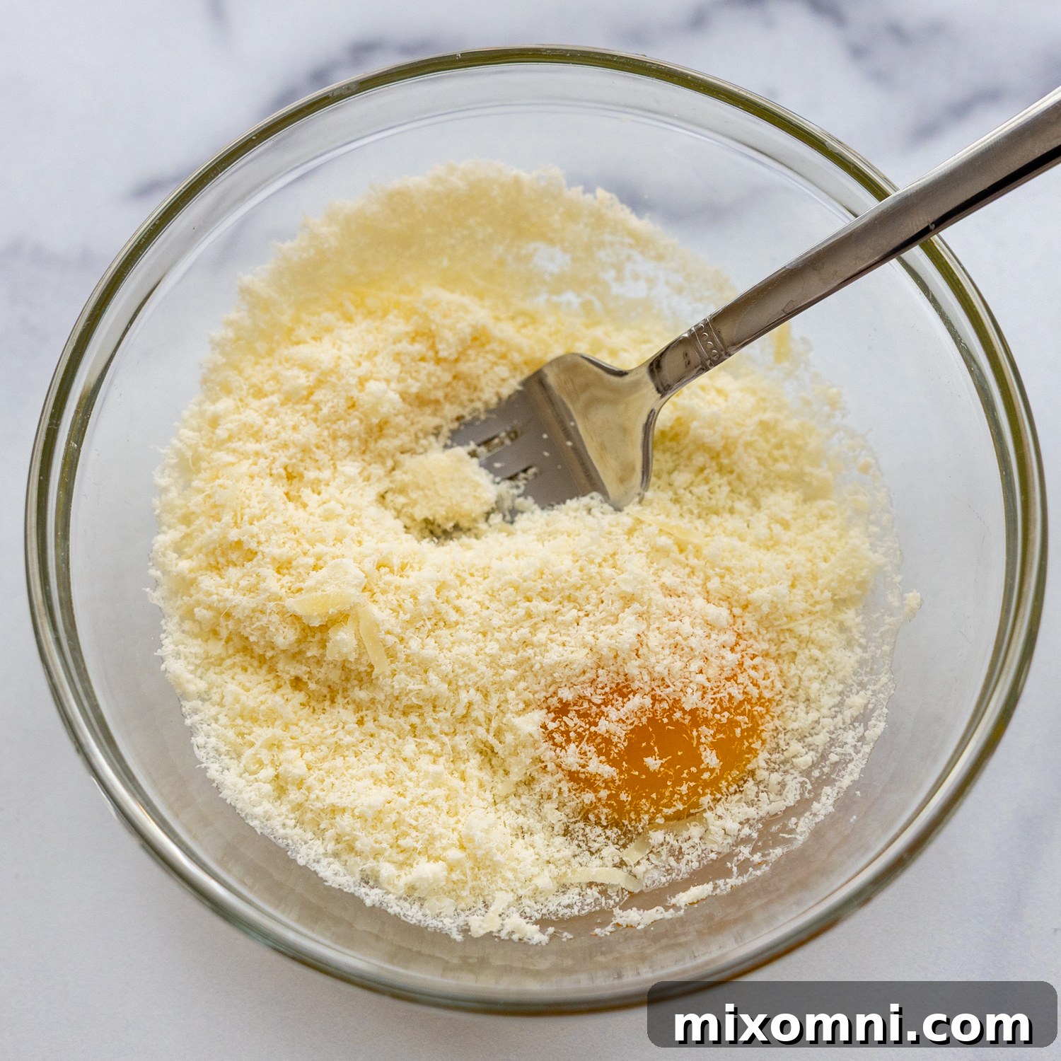 Whisked egg and grated parmesan cheese in a small glass bowl, ready to be added to the soup.