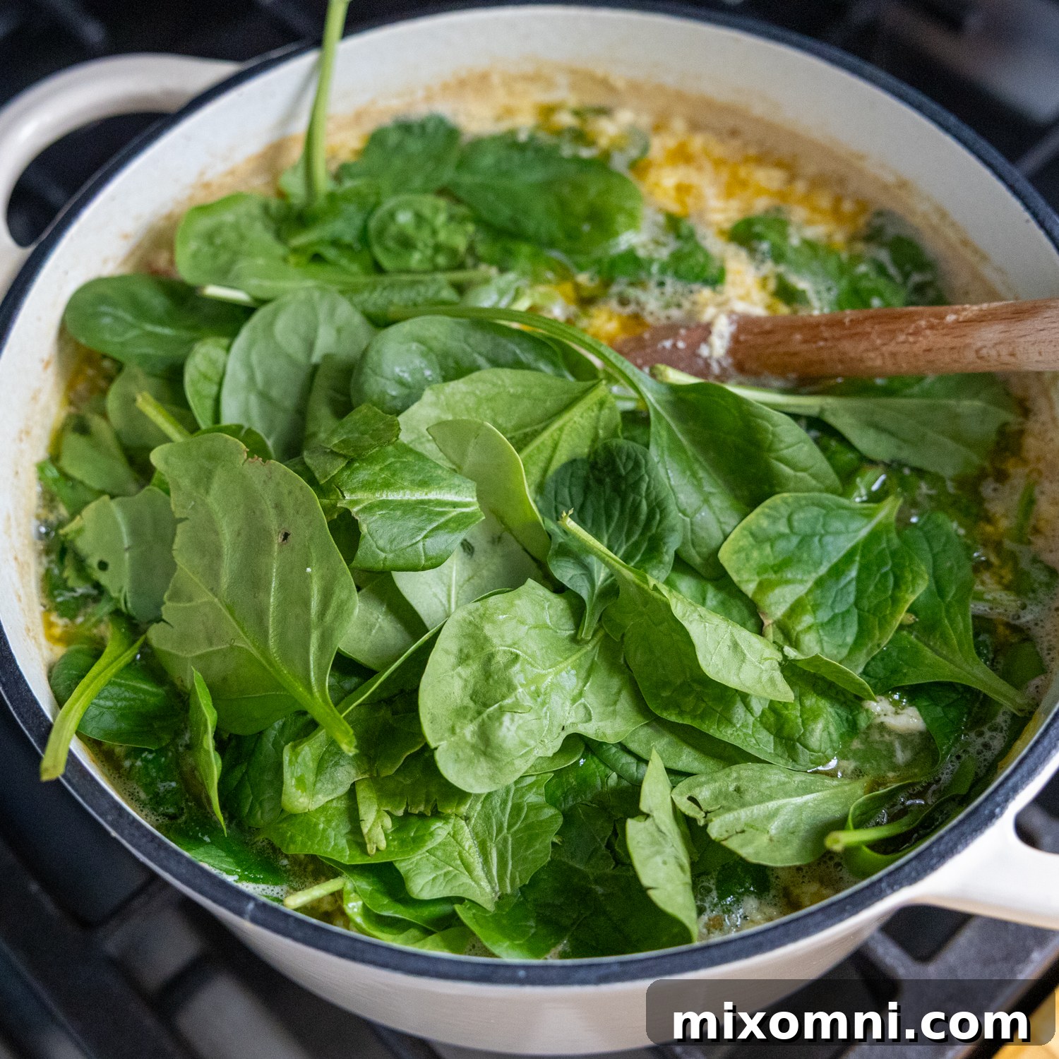 Fresh spinach being gently folded into a pot of Italian Wedding Soup.