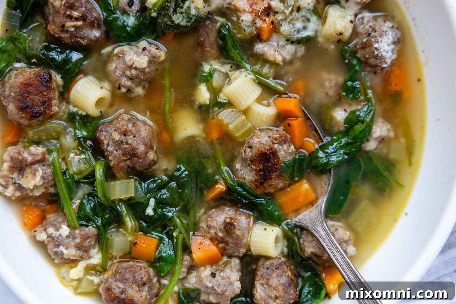 A serving of Gluten Free Italian Wedding Soup in a white bowl with a spoon.