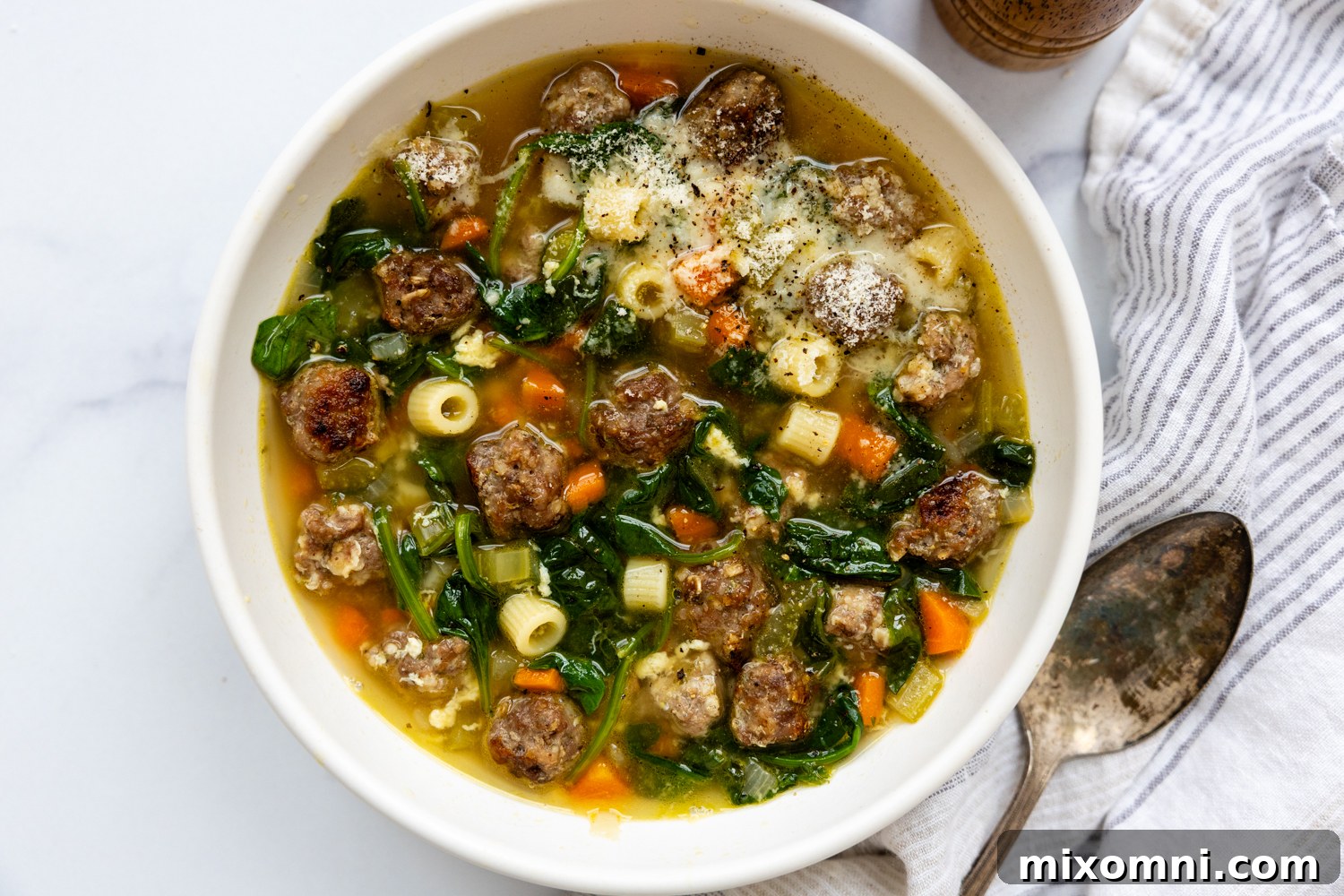 A white bowl of Italian Wedding Soup with a spoon resting beside it, on a wooden surface.