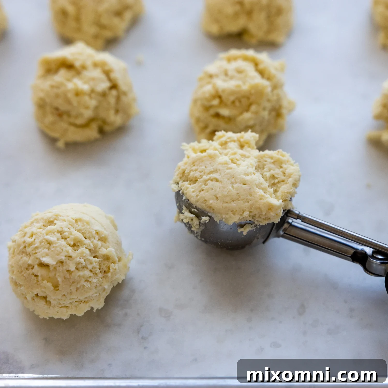 Biscuits dough being scooped and dropped onto parchment paper.