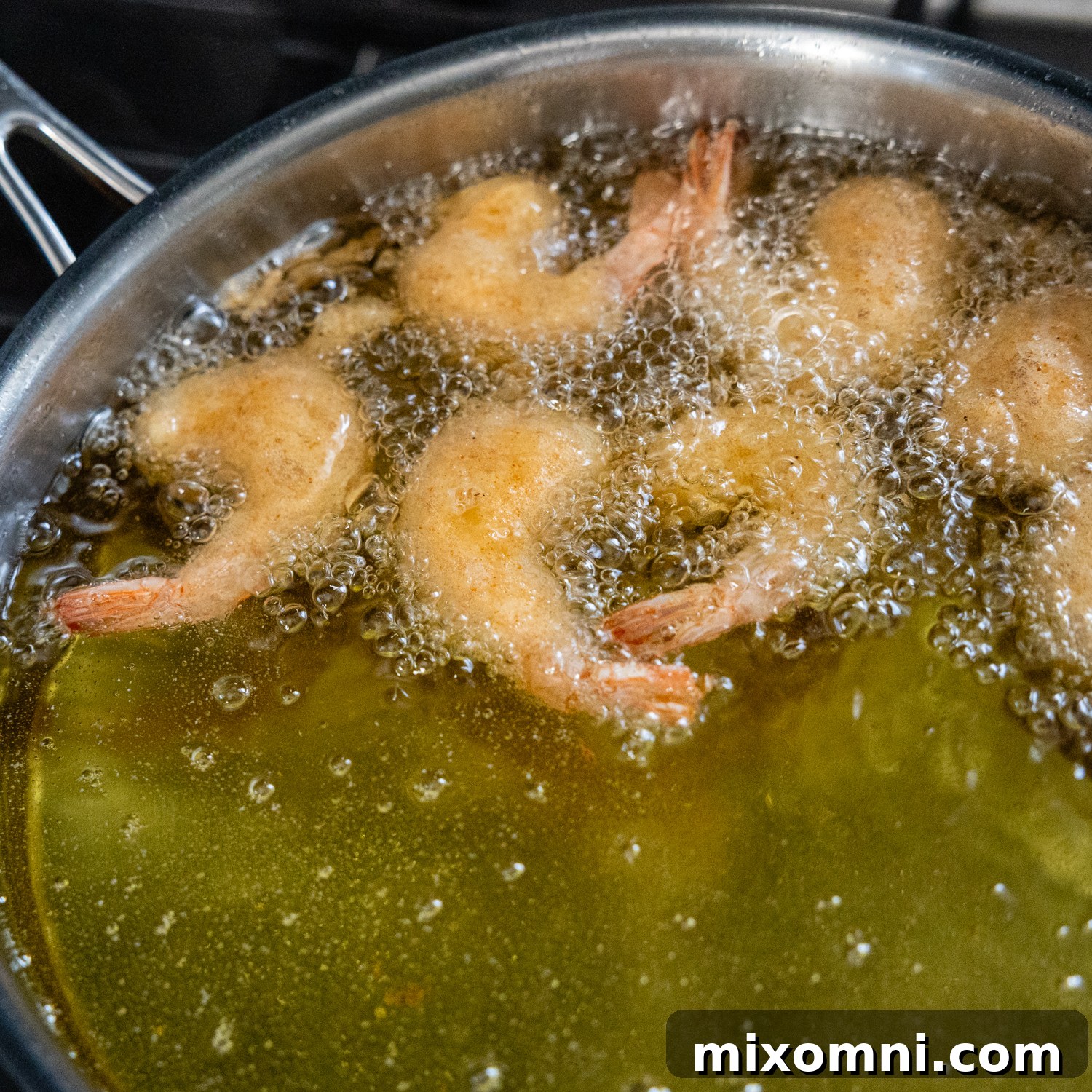Several battered shrimp frying to a golden crisp in hot oil within a skillet.