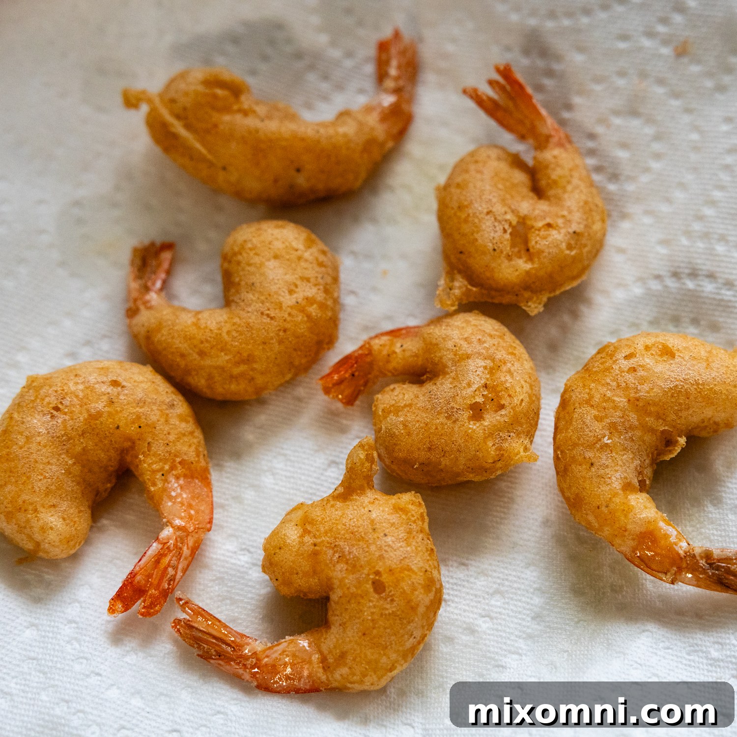 Freshly fried, crispy shrimp resting on paper towels to drain excess oil after frying.