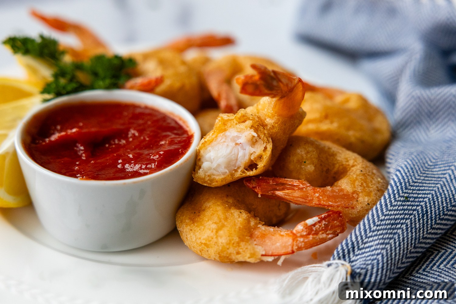 Vertical image showing a close-up, inside view of a piece of perfectly battered and fried shrimp, revealing the succulent meat and crisp coating.