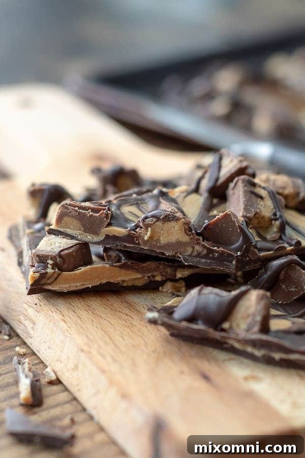 A side angle photo of the beautiful tiger butter candy on a wooden cutting board, showcasing its swirled layers and toppings.
