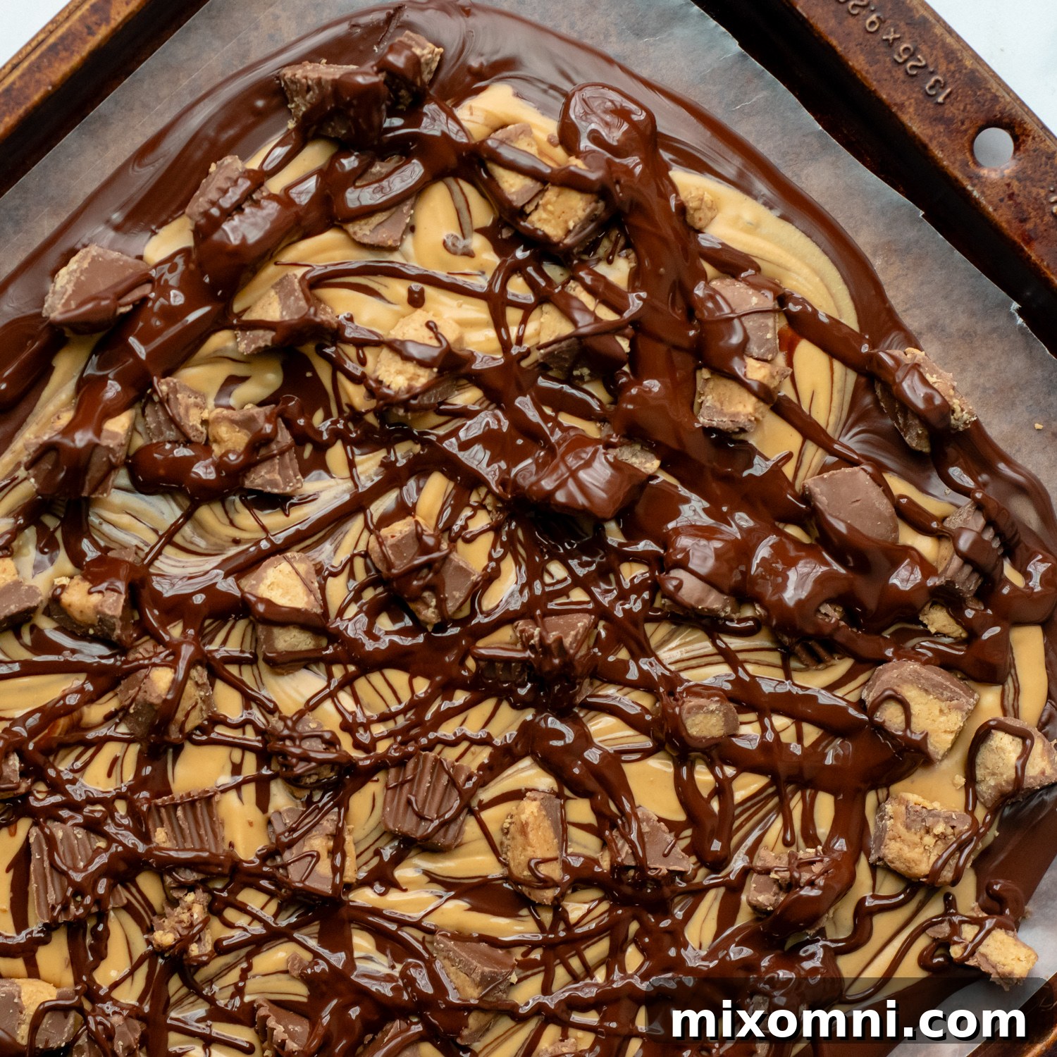 Melted chocolate drizzled over the top of the peanut butter chocolate mixture with chopped cups, securing the toppings.