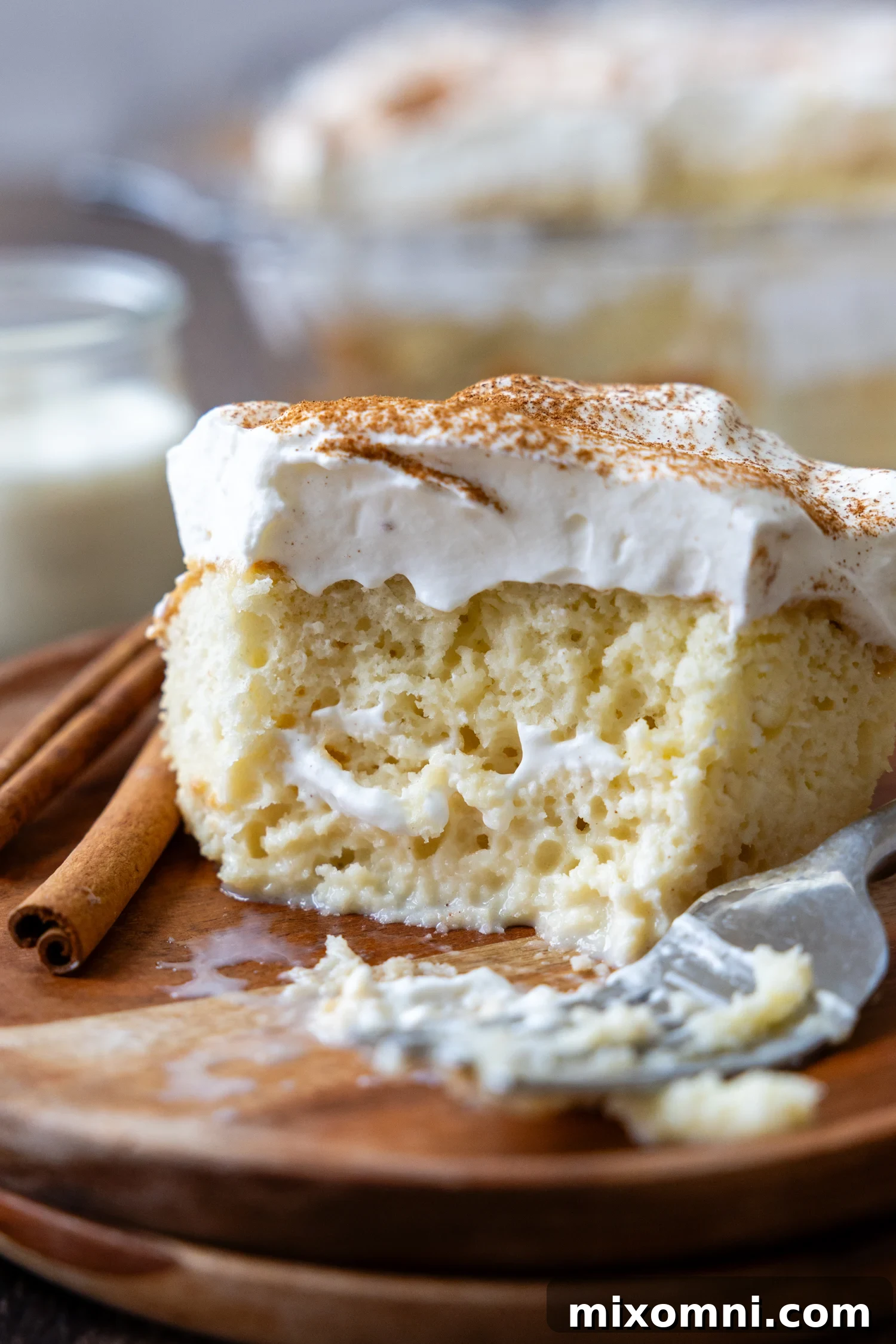 A perfectly moist slice of gluten-free tres leches cake on a wooden plate with a bite removed, showcasing its light and airy texture.