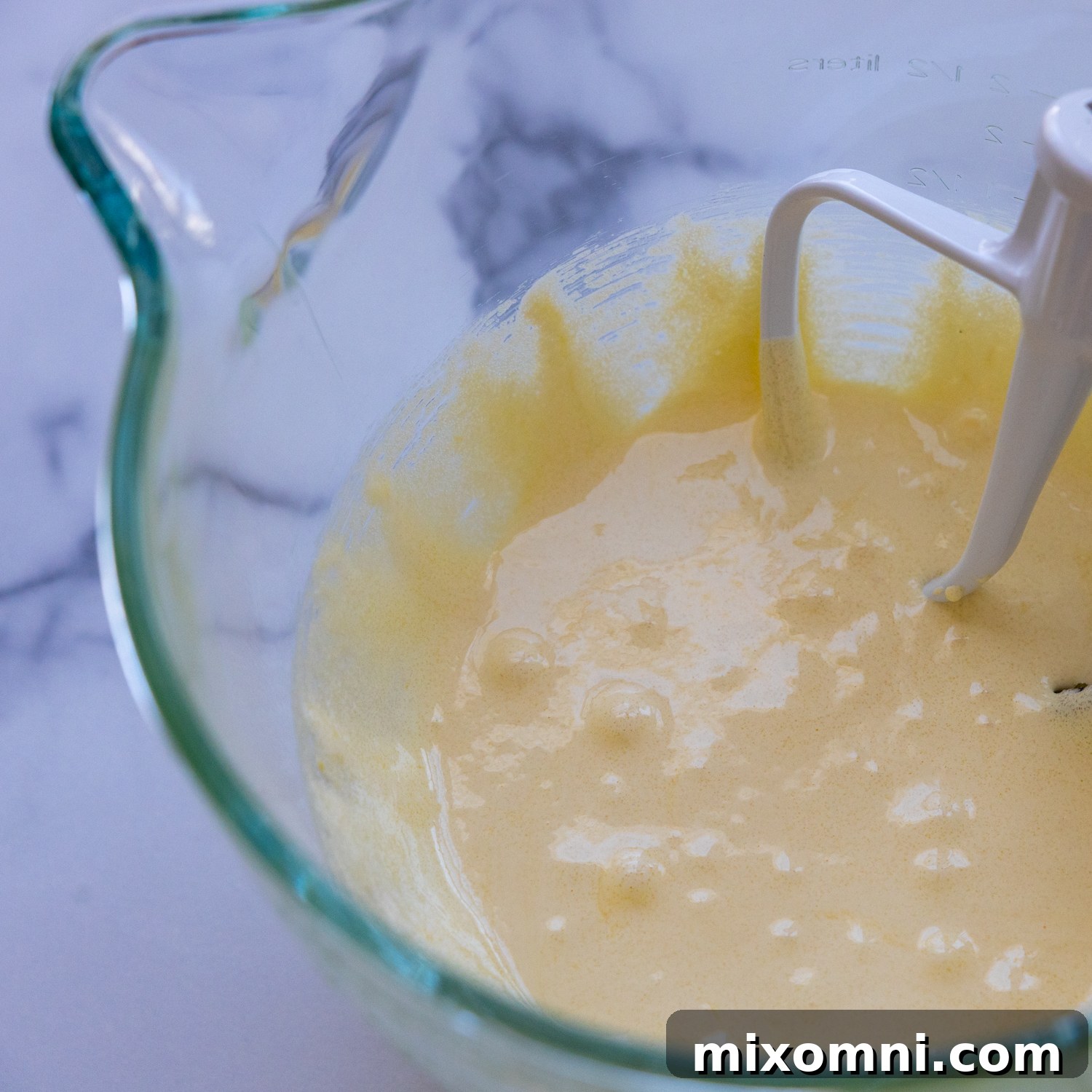 Creamy, pale yellow egg yolk and sugar mixture being beaten in a glass bowl.