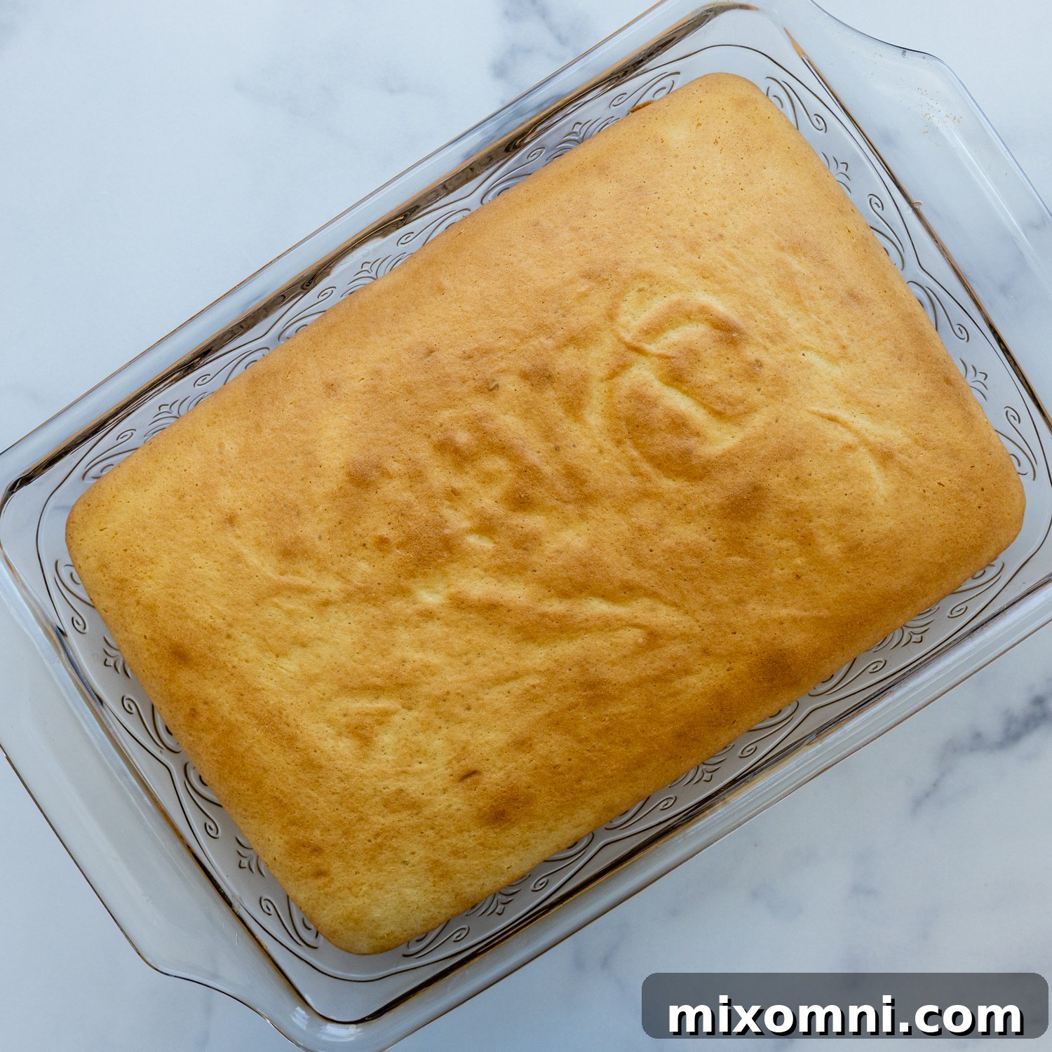 A freshly baked gluten-free tres leches cake cooling in a glass baking pan.