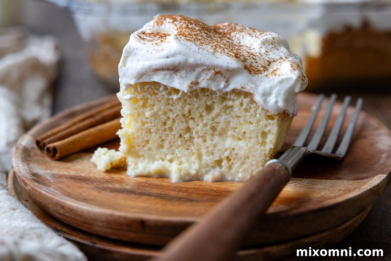 A slice of gluten-free tres leches cake with a fork on a wooden plate, ready to be enjoyed.