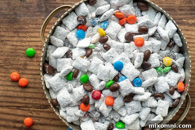 An overhead shot of Nutella puppy chow in a silver bowl with colorful M&Ms scattered nearby.