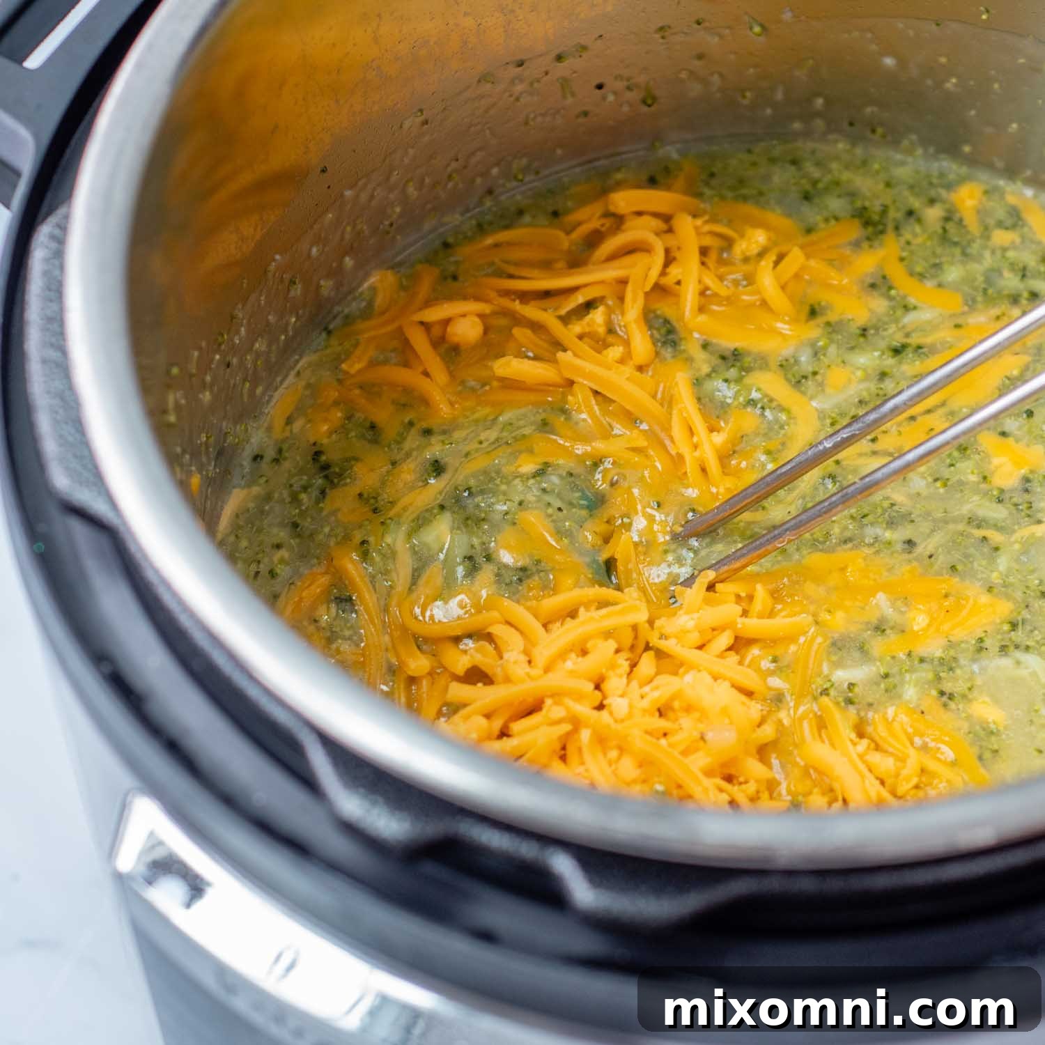 Stirring in freshly shredded cheddar cheese and half and half into the broccoli soup, making it creamy.