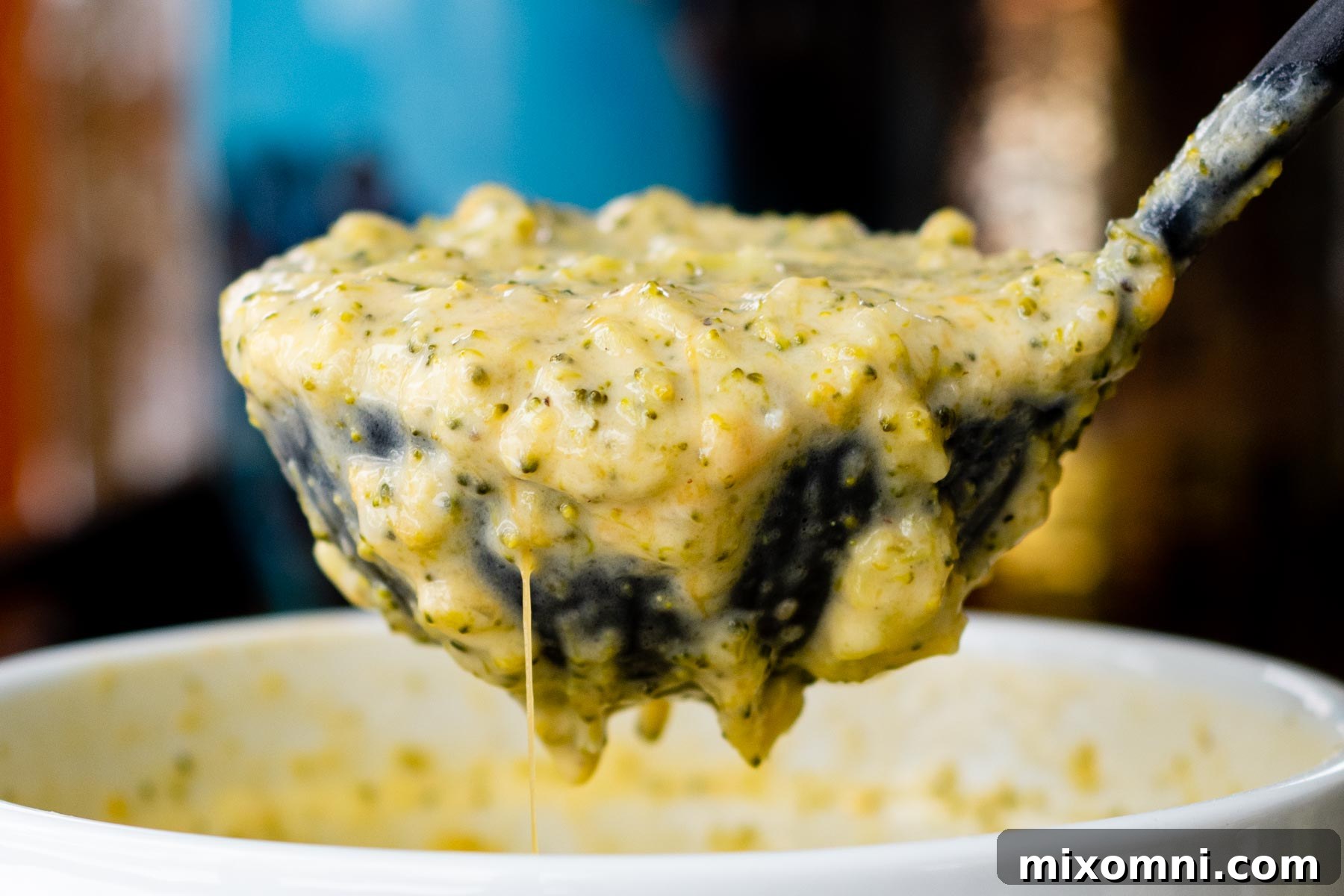 A close-up of a spoon lifting a perfect bite of creamy broccoli cheddar soup, garnished with a sprinkle of fresh herbs.