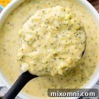 overhead shot of a ladle holding up broccoli cheese soup, ready to serve