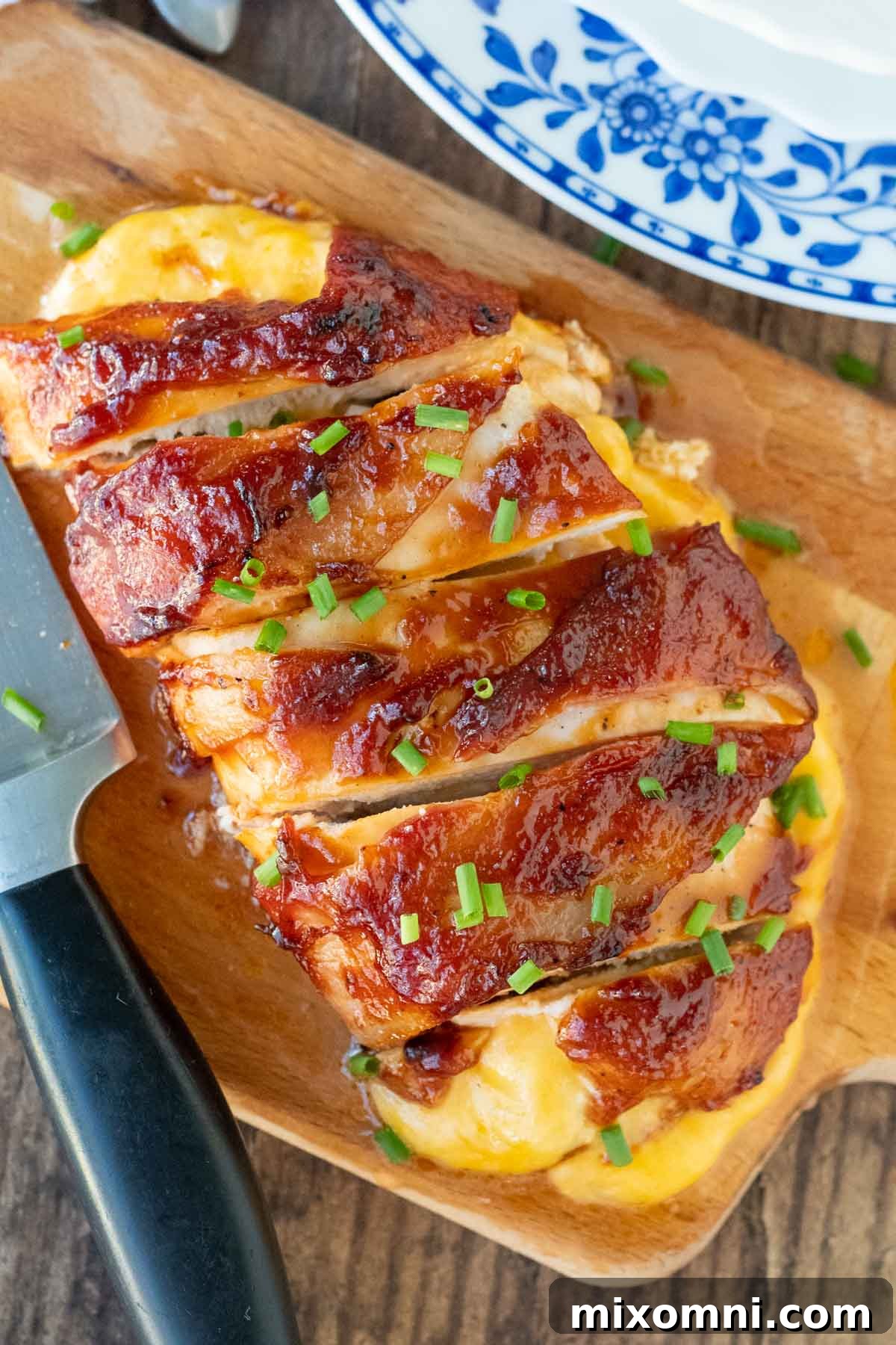 Overhead shot of golden-brown BBQ bacon wrapped chicken, garnished with fresh chives, oozing with melted cheese.
