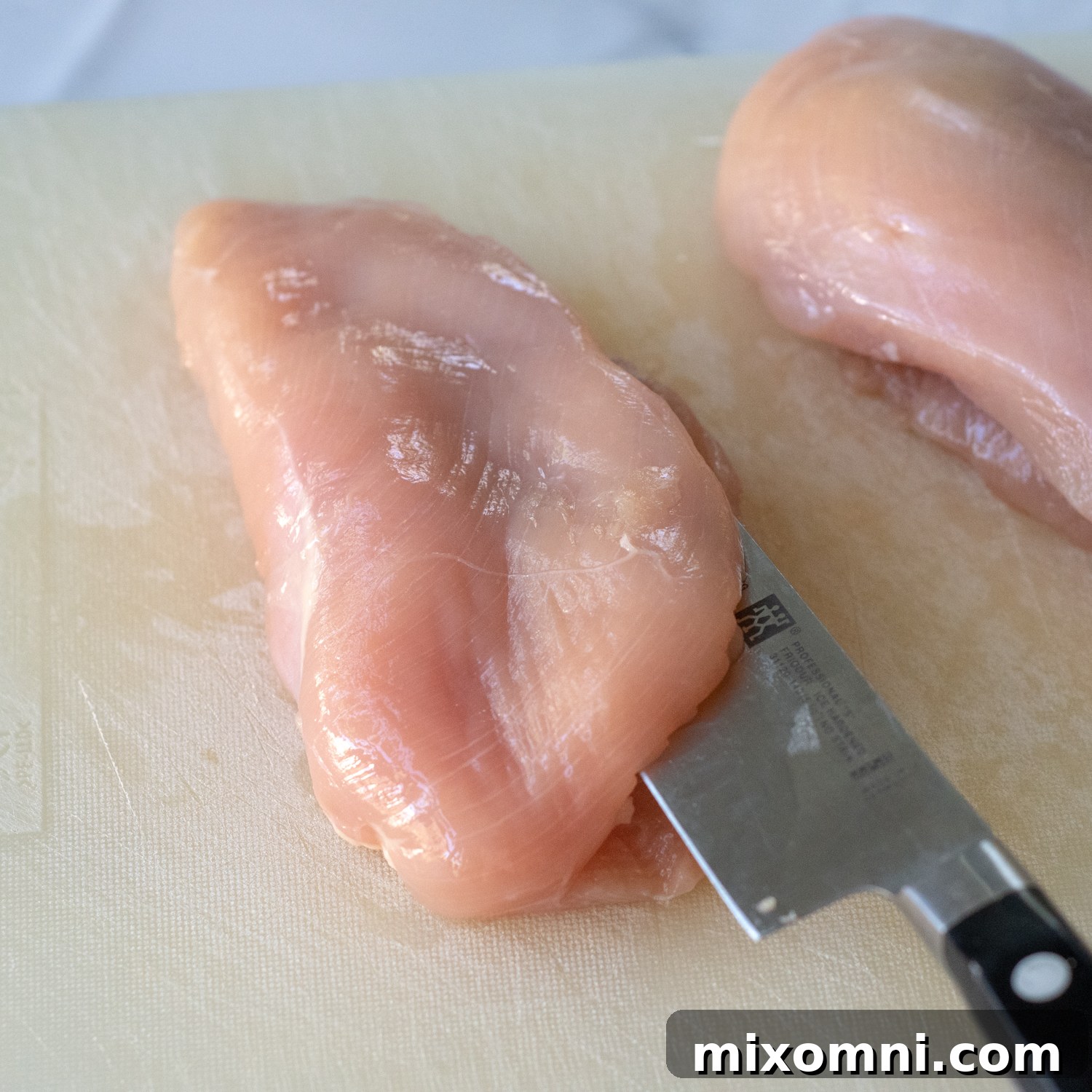 A sharp knife carefully slicing into a raw chicken breast to create a pocket for stuffing.