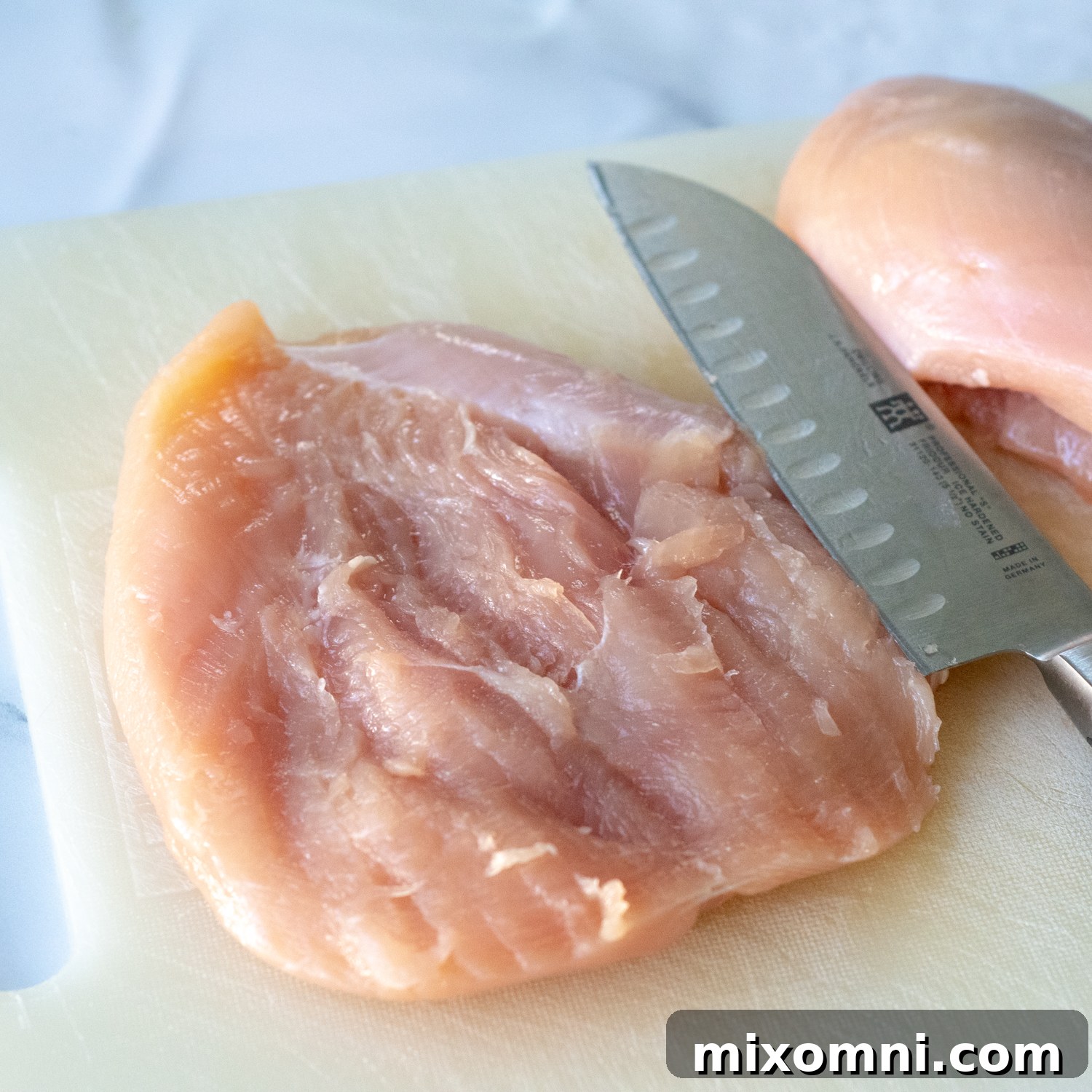 A butterflied chicken breast lying open on a cutting board, ready for its cheesy filling.