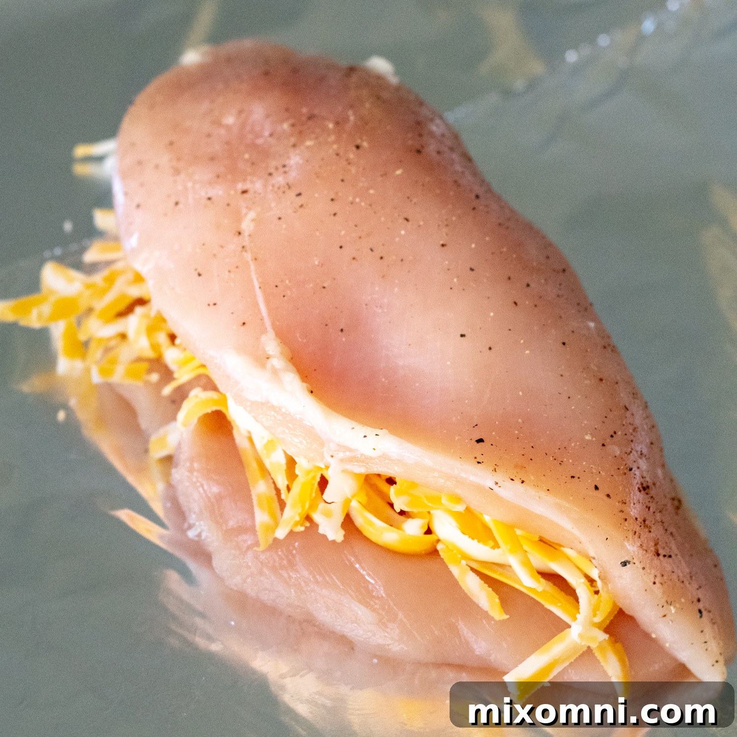 Raw chicken breast, butterflied and filled with a mound of shredded cheese, ready to be folded.