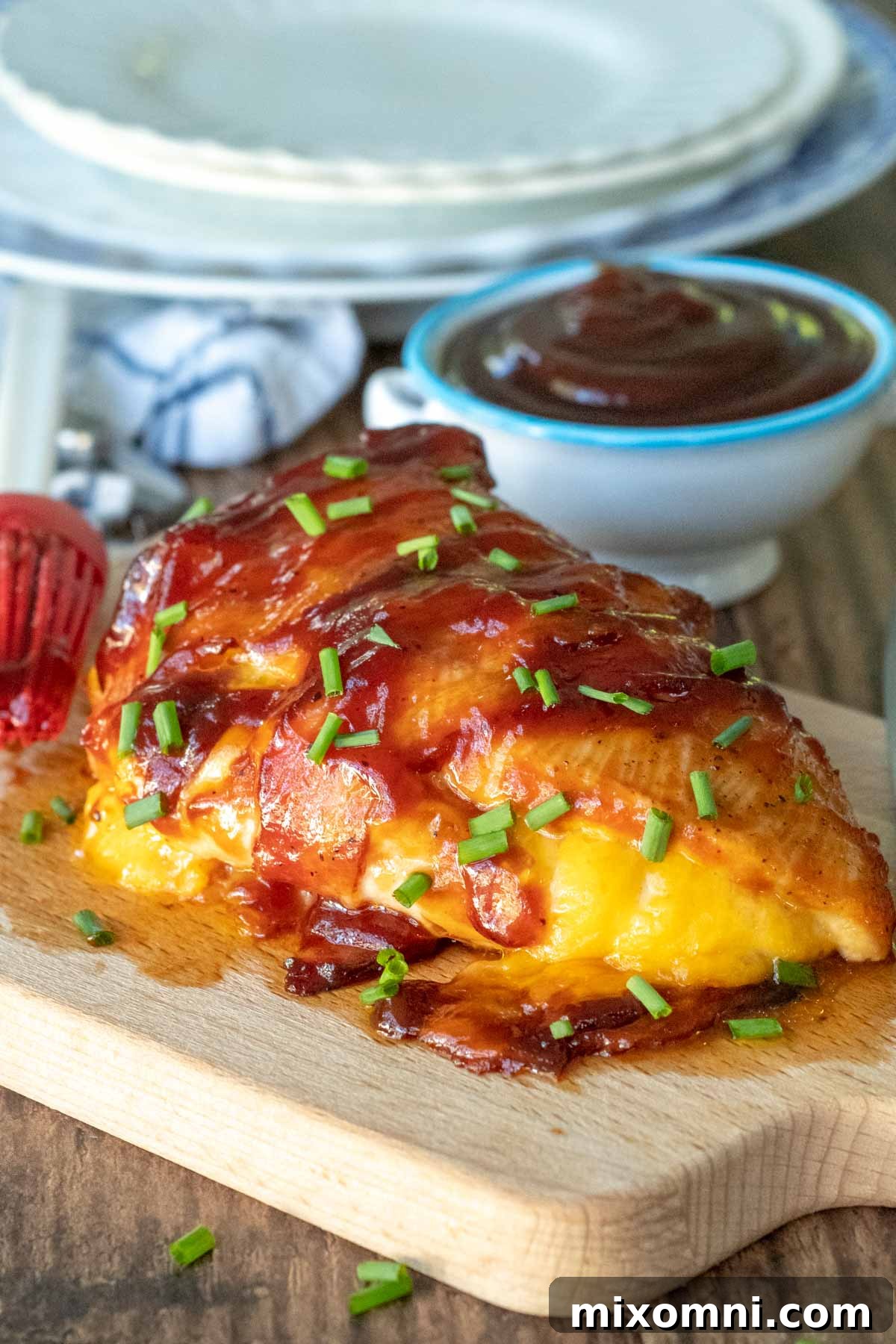 A perfectly cooked BBQ bacon wrapped chicken breast, golden and glazed, on a rustic wooden cutting board.