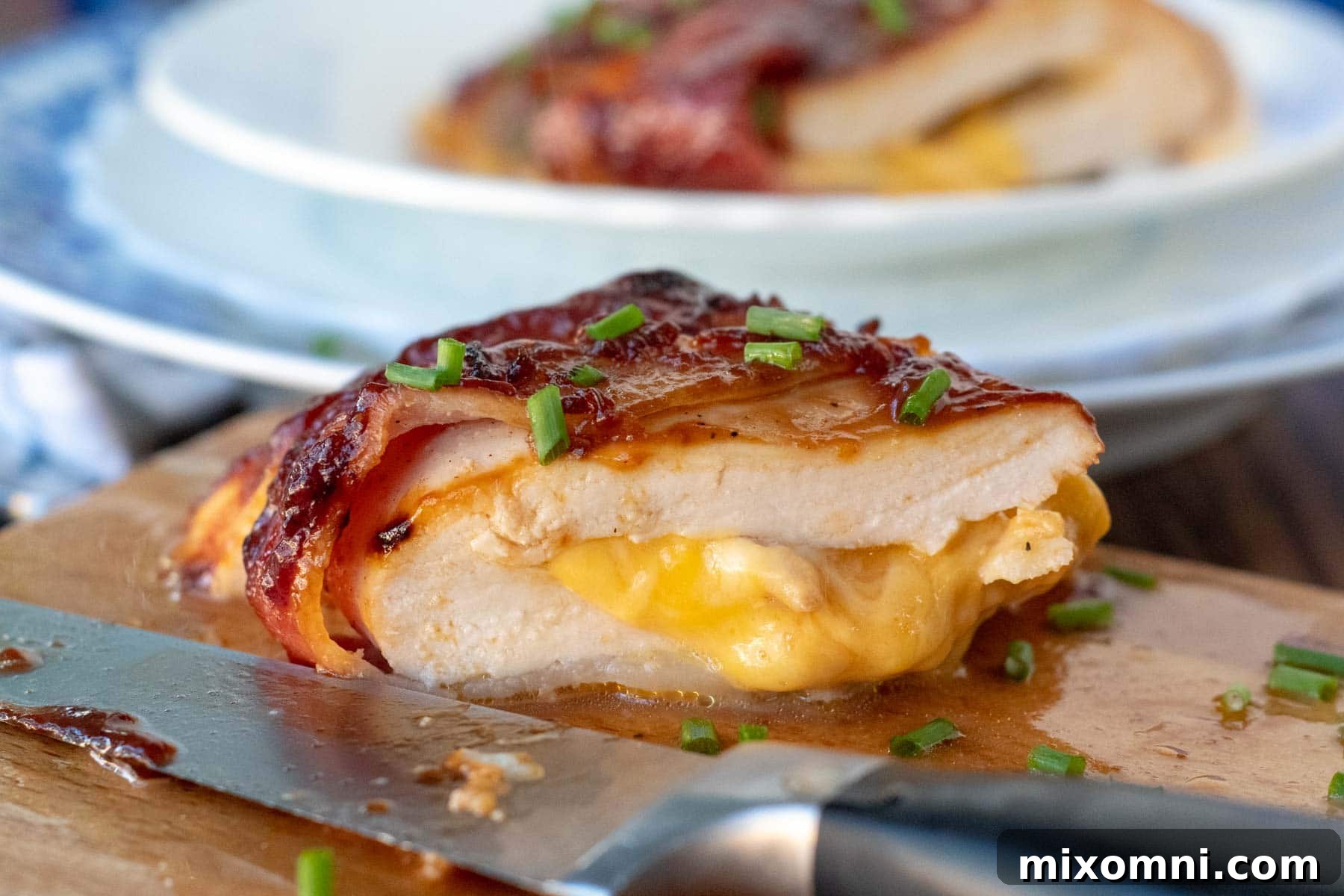 Close-up of baked bacon wrapped chicken, cut open to reveal luscious, oozing melted cheese inside.