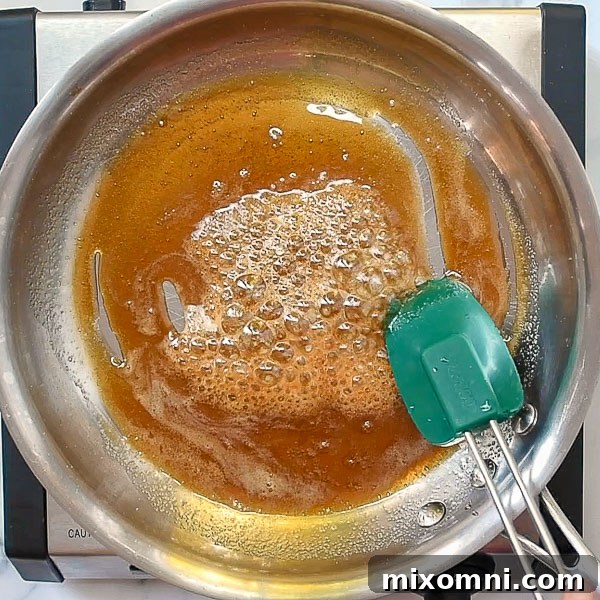 First step of how to make candied pecans: bring brown sugar, maple syrup, water, and salt to a boil in a skillet.