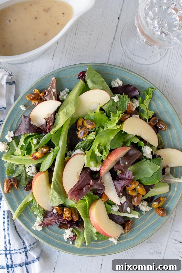 an overhead shot of harvest salad on a blue plate with a wine class and container of dressing next to it