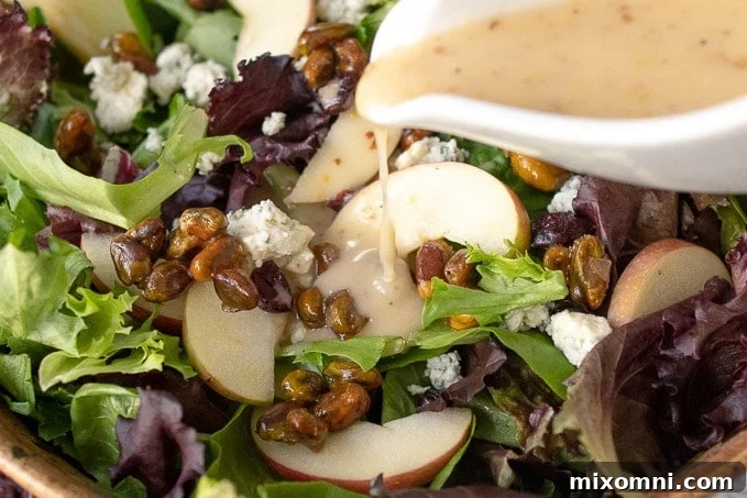 an up close shot of maple vinaigrette being poured from a white dressing container onto the harvest salad