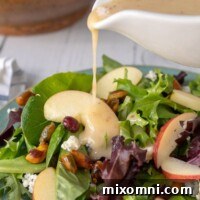 maple vinaigrette being poured from a white dressing container onto the apple pecan salad