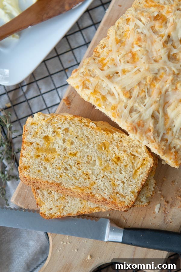 An overhead shot of a golden-brown, sliced quick cheese bread on a wooden cutting board, revealing melted cheddar within.