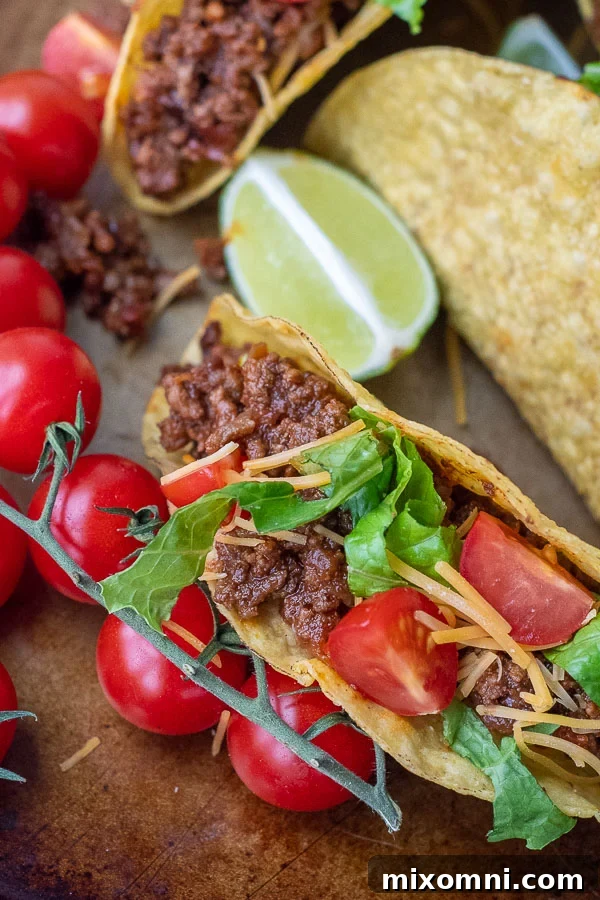 Close up of a beef taco generously filled with sweet and spicy sloppy joe meat, topped with fresh tomatoes, shredded cheese, and crisp lettuce.
