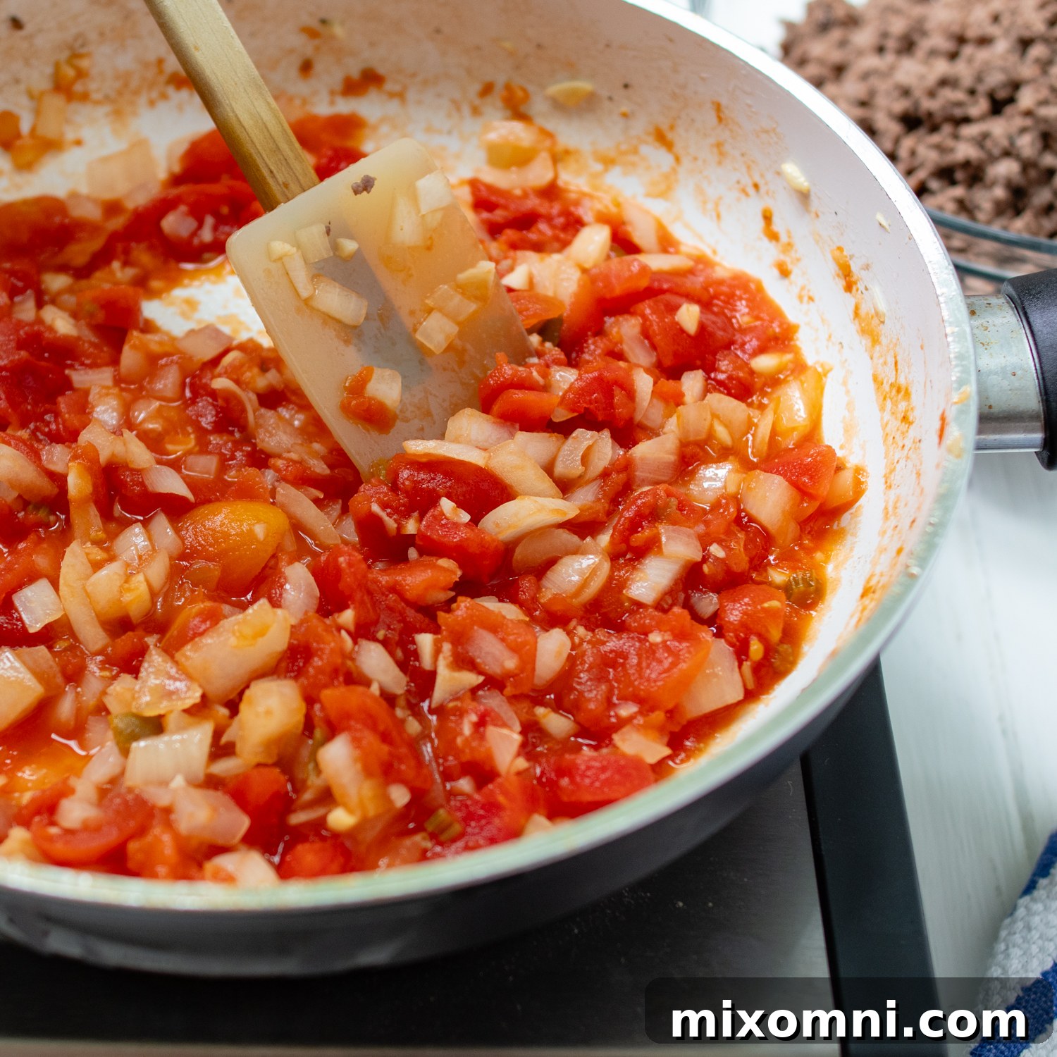 Sautéed stewed tomatoes and onions simmering in a skillet, creating an aromatic foundation for the taco filling.