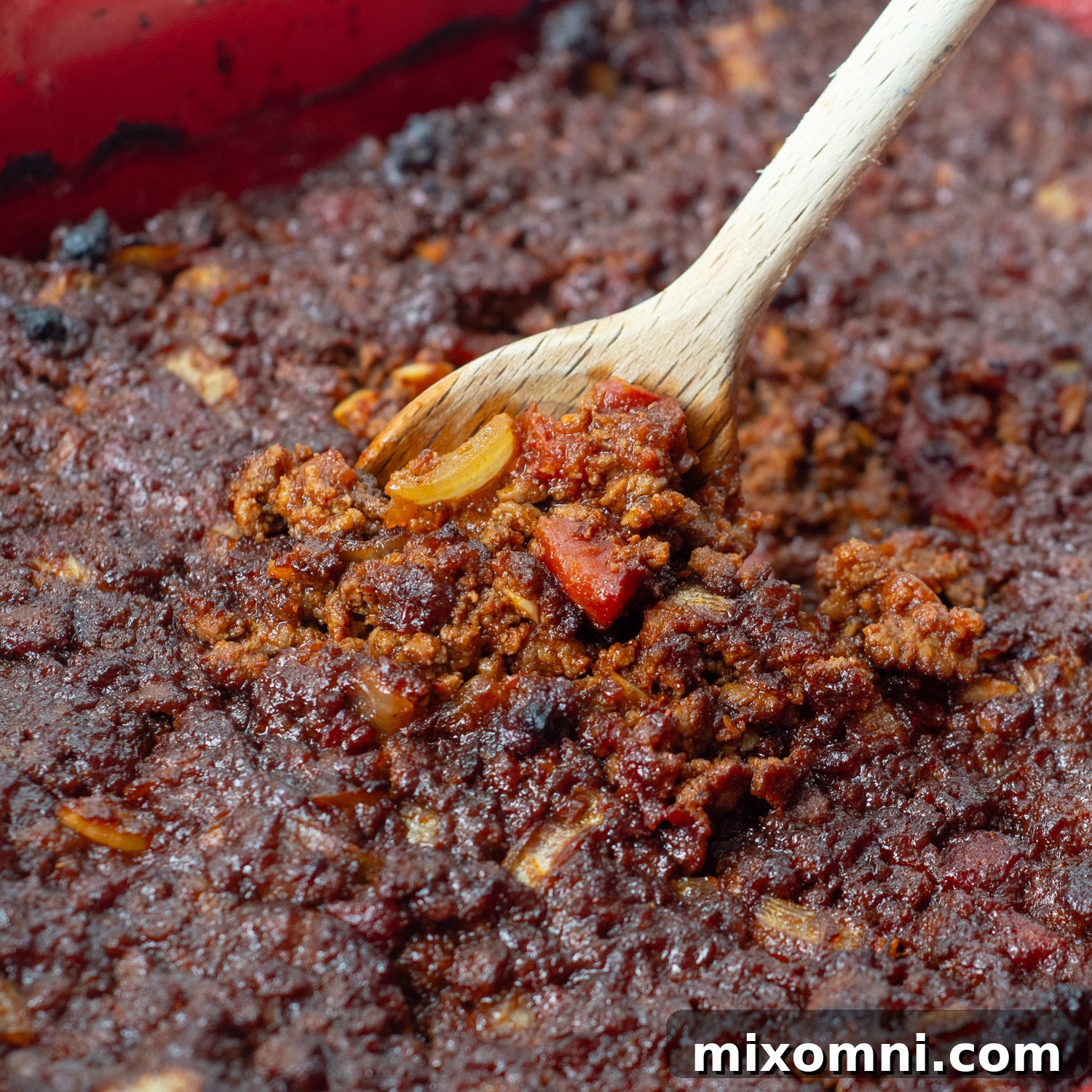 Baked taco meat resting in a baking pan, with a wooden spoon lifting a portion, showcasing the rich, dark crust formed around the edges.