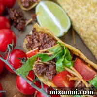 Close up of a beef taco generously filled with sweet and spicy sloppy joe meat, topped with fresh tomatoes, shredded cheese, and crisp lettuce.